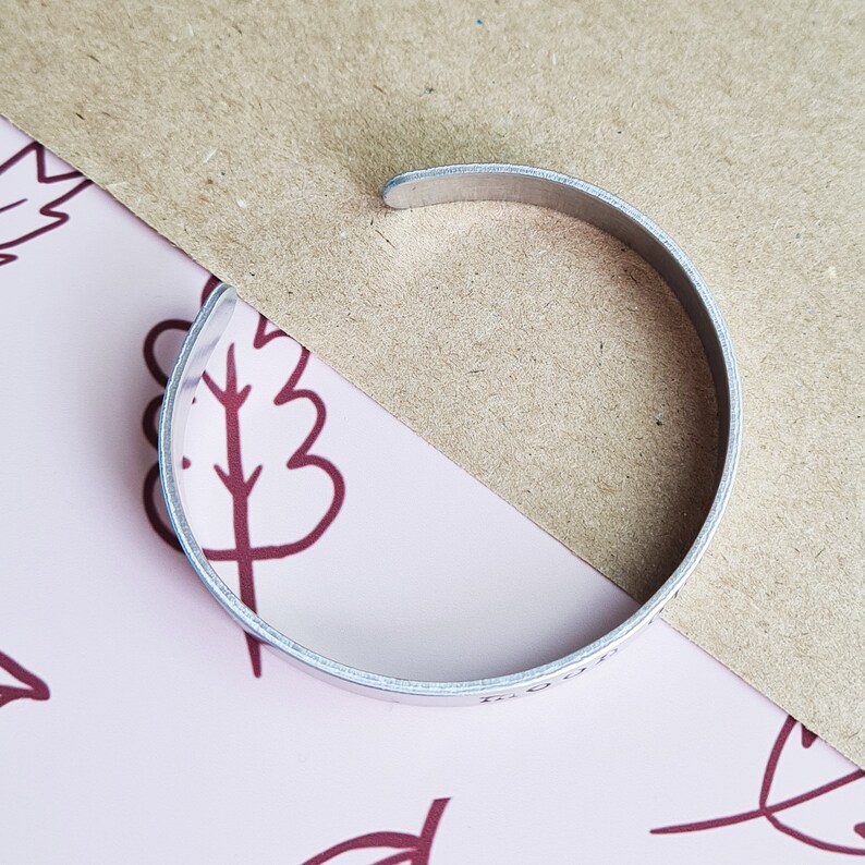 May include: A silver metal bangle bracelet with a smooth, rounded surface. The bracelet is engraved with the words "Forever Young".
