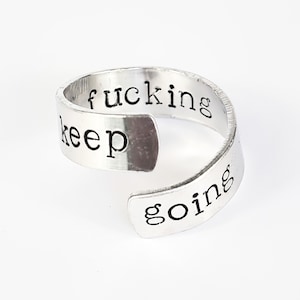 May include: A silver ring with the words "keep fucking going" engraved on it.