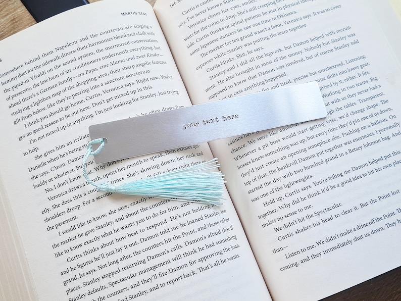 May include: A silver metal bookmark with a light blue tassel. The bookmark has the text "your text here" printed on it.