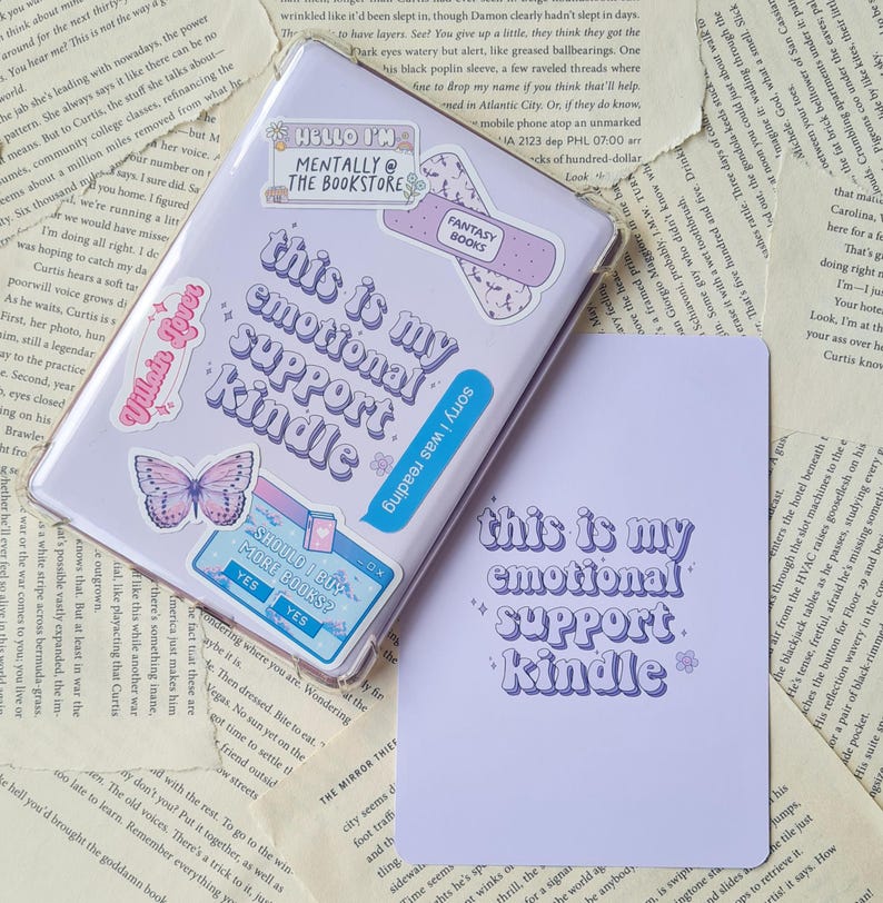 Puede incluir: Una funda morada para Kindle con el texto "This is my emotional support Kindle" en una fuente azul y morada. La funda est&aacute; decorada con pegatinas de mariposas, un libro y un cuadro de texto que dice "Should I buy more books?" con un bot&oacute;n de s&iacute;.