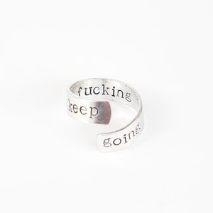 May include: Silver ring with the words "keep fucking going" engraved on it.