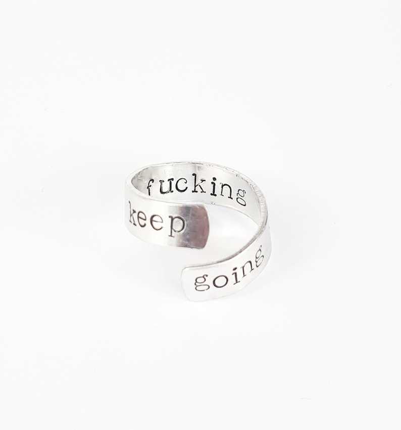 May include: Silver ring with the words "keep fucking going" engraved on it.