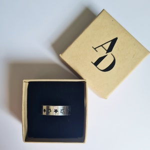 May include: A silver ring with a black star design on a black velvet background in a brown box with the letters "AD" printed on the top.