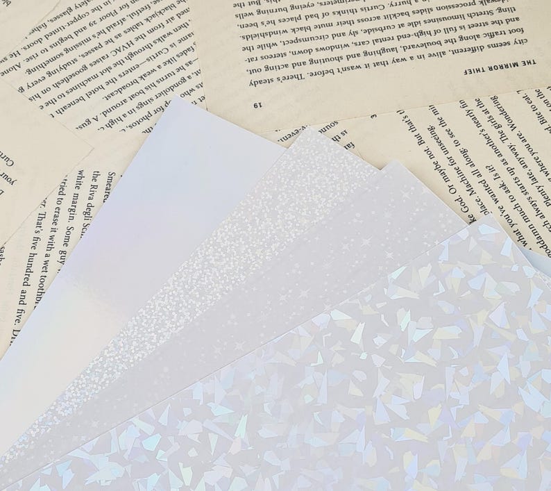 Puede incluir: Primer plano de tres papeles blancos diferentes con varios patrones. El papel de abajo tiene un patr&oacute;n hologr&aacute;fico de peque&ntilde;as formas iridiscentes. El papel del medio tiene un patr&oacute;n sutil y moteado. El papel de arriba es blanco liso.