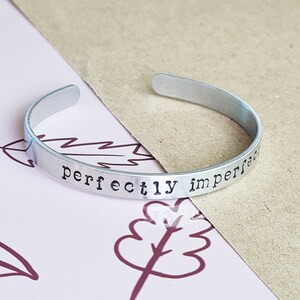 May include: Silver bangle bracelet with the words "perfectly imperfect" engraved on it.