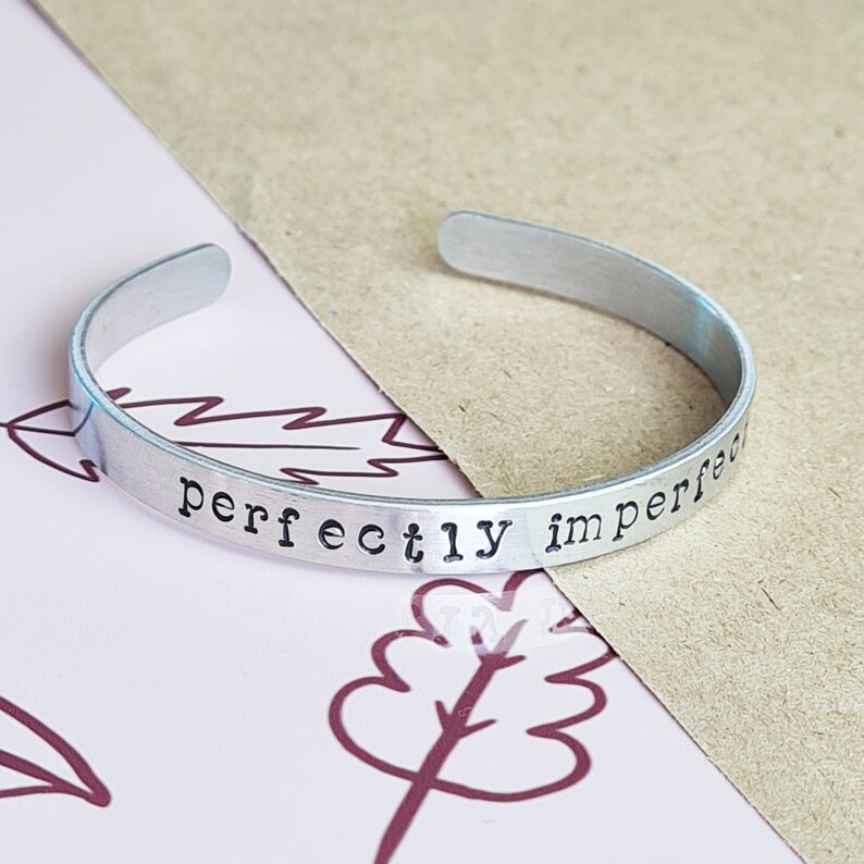 May include: Silver bangle bracelet with the words "perfectly imperfect" engraved on it.