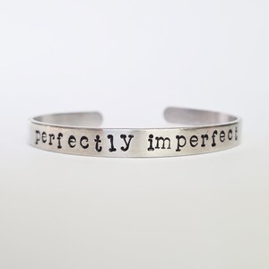 May include: Silver bracelet with the words "perfectly imperfect" engraved on it.