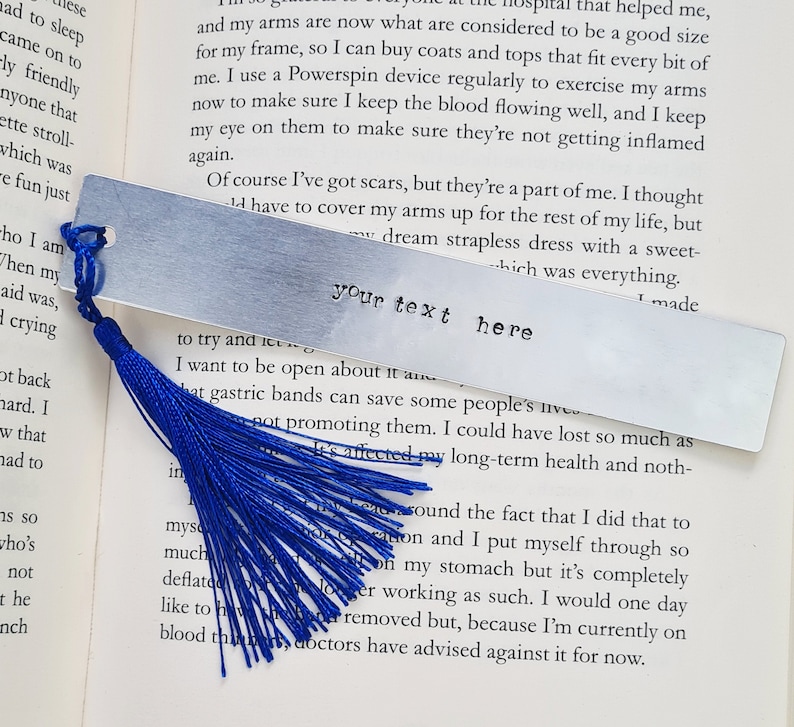 May include: A silver bookmark with a blue tassel. The bookmark is rectangular and has the text "your text here" engraved on it.