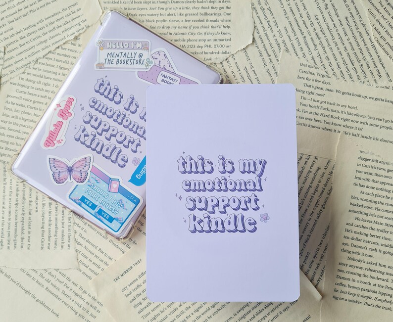 Puede incluir: Cuaderno morado y blanco con el texto "This is my emotional support kindle" en una fuente retro. El cuaderno tiene una cubierta de color morado claro y est&aacute; decorado con pegatinas.