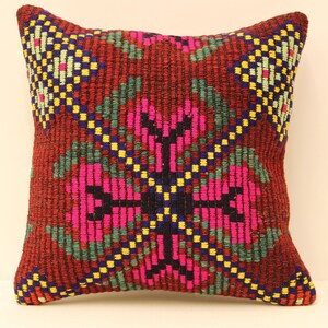 May include: A square pillow with a red background and a colorful geometric pattern. The pattern features pink, green, blue, yellow, and black squares and rectangles. The pillow is made of a woven fabric and has a fringed edge.