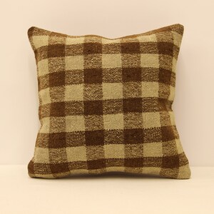 May include: Square decorative pillow with a brown and tan checkered pattern. The pillow has a woven texture and a neutral color palette, suitable for various home decor styles. The pillow is a square shape.