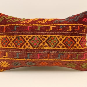 May include: A rectangular pillow with a colorful geometric pattern in shades of red, orange, yellow, green, and blue. The pillow is made of woven fabric and has a fringed edge.