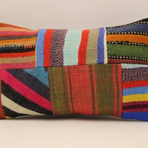 Può includere: Un cuscino rettangolare colorato in patchwork. Il cuscino è realizzato con diversi tessuti con strisce e motivi geometrici in tonalità di rosso, blu, verde, giallo, rosa e nero.