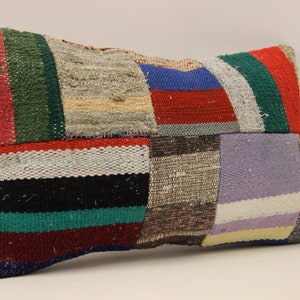 Op de afbeelding: Een rechthoekig patchwork kussen met verschillende kleuren en patronen, waaronder rood, groen, blauw, wit en zwart. Het kussen is gemaakt van geweven stof en heeft een licht getextureerd oppervlak.