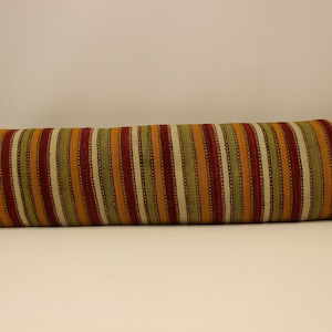 May include: A long, rectangular pillow with a striped pattern in shades of red, orange, green, and cream. The pillow is made of a woven fabric and has a slightly textured surface.