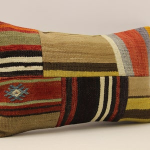 Könnte beinhalten: Ein rechteckiges Kissen mit Patchwork-Muster. Das Kissen besteht aus verschiedenen Stoffen in den Farben Rot, Braun, Gelb und Weiß. Das Kissen hat ein geometrisches Muster in der Mitte.