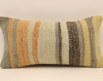 May include: A long, rectangular pillow with a striped pattern in shades of gray, beige, orange, and brown. The pillow is made of woven fabric and has a rustic, hand-crafted look.
