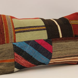 Può includere: Un cuscino rettangolare in patchwork con una varietà di colori e motivi, tra cui rosso, marrone, verde, blu e rosa. Il cuscino è realizzato in tessuto tessuto e ha una superficie leggermente strutturata.