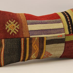 May include: A colourful patchwork cushion with a variety of woven patterns in shades of red, brown, green, and beige. The cushion is made of a soft, textured fabric and has a rectangular shape.
