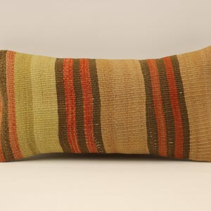 May include: A long, rectangular pillow with a striped pattern in shades of brown, beige, and orange. The pillow is made of a woven fabric with a slightly textured surface.