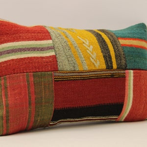 Op de afbeelding: Een kleurrijk patchwork kussen met strepen en geometrische patronen in tinten rood, groen, geel, blauw en zwart.