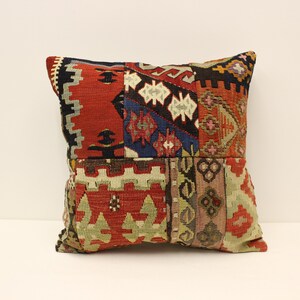 Puede incluir: Una funda de cojín de patchwork con una variedad de patrones geométricos coloridos en tonos de rojo, azul, verde y marrón. La funda de cojín está hecha de tejido tejido y tiene un borde con flecos.