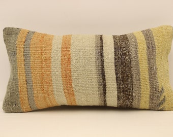 May include: A long, rectangular pillow with a striped pattern in shades of gray, beige, orange, and brown. The pillow is made of woven fabric and has a slightly textured surface.