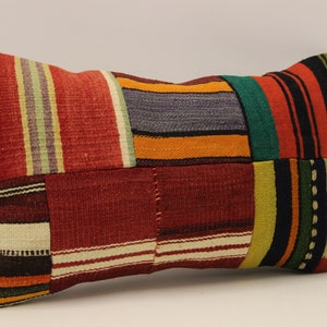 Può includere: Un cuscino rettangolare in patchwork con una varietà di strisce colorate in rosso, arancione, giallo, verde, blu e nero.