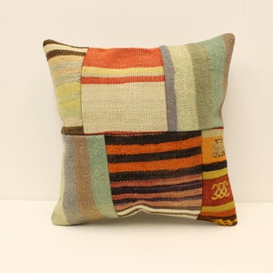 Puede incluir: Una funda de cojín de patchwork con una variedad de colores y patrones, incluyendo naranja, marrón, beige y verde. La funda de cojín está hecha de tejido tejido y tiene una forma cuadrada.