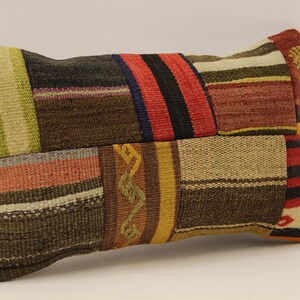 Può includere: Un cuscino rettangolare in patchwork con una varietà di colori e motivi, tra cui rosso, verde, marrone e giallo.