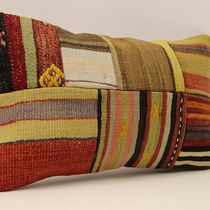 Può includere: Un cuscino rettangolare in patchwork con una varietà di colori e motivi, tra cui rosso, marrone, giallo e verde. Il cuscino è realizzato in tessuto tessuto e ha una superficie leggermente strutturata.