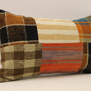 Può includere: Un cuscino rettangolare in patchwork con un motivo a quadri marroni, neri, bianchi, arancioni e blu. Il cuscino è realizzato in tessuto tessuto e ha una texture morbida e confortevole.