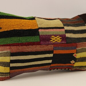 Puede incluir: Una almohada de patchwork colorida con un diseño a rayas en tonos de rojo, naranja, amarillo, verde, azul y negro. La almohada está hecha de tejido tejido y tiene una forma rectangular.