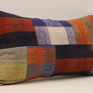 May include: Rectangular patchwork pillow with a variety of colors and patterns. The pillow features squares and stripes in shades of red, blue, orange, and green. The pillow is made of a woven fabric.