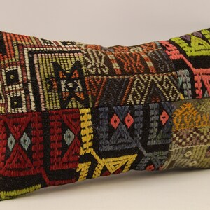 May include: A colorful rectangular pillow with a patchwork design featuring geometric patterns in shades of red, green, yellow, blue, and brown.
