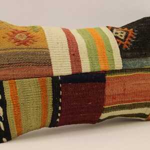 Op de afbeelding: Een rechthoekig kussen met een patchwork-ontwerp. Het kussen is gemaakt van verschillende gekleurde stoffen, waaronder rood, groen, bruin en wit. De stof is geweven met strepen en patronen.