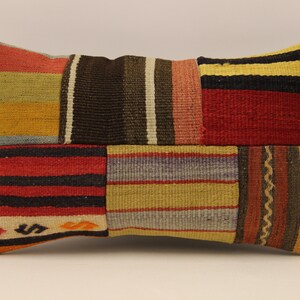 Può includere: Un cuscino rettangolare in patchwork con una varietà di strisce colorate in rosso, giallo, arancione, nero, marrone e grigio.