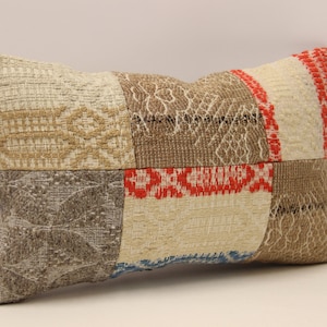 May include: Rectangular decorative pillow with a patchwork design. The pillow features various textured fabric squares in beige, brown, red, and gray. The pillow's design includes geometric and patterned elements, creating a rustic aesthetic.
