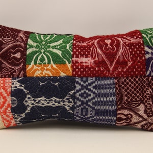 Può includere: Un cuscino rettangolare con un design a patchwork. Il cuscino è realizzato con diversi tessuti con vari motivi e colori, tra cui rosso, verde, blu, arancione e bianco.