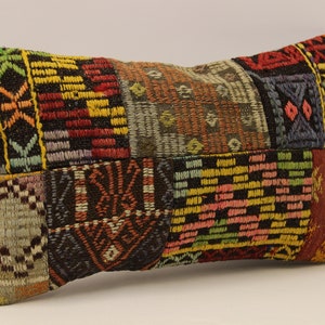 Puede incluir: Una almohada rectangular de patchwork colorida con intrincados patrones geométricos en tonos rojos, amarillos, verdes, azules y marrones.