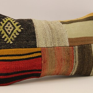 May include: A rectangular patchwork cushion with a geometric design in the centre. The cushion is made of different coloured fabrics, including black, brown, red, and yellow.