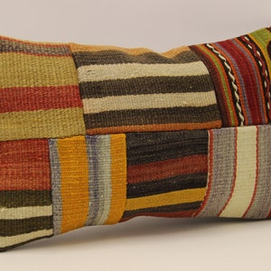 May include: A rectangular cushion with a patchwork design. The cushion is made of different coloured fabrics with striped patterns in shades of red, orange, yellow, green, brown, and white.