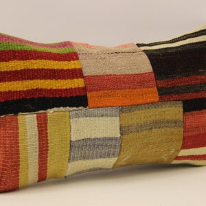 Puede incluir: Una almohada de patchwork colorida con rayas rojas, naranjas, amarillas, verdes, azules y marrones. La almohada está hecha de tejido tejido y tiene una forma rectangular.