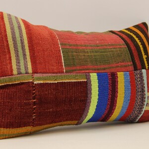 May include: A rectangular patchwork cushion with a variety of colourful stripes in red, green, blue, yellow, and brown. The cushion is made of woven fabric and has a rustic, handmade look.