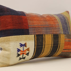 Peut inclure: Un coussin rectangulaire en patchwork avec un motif rayé beige, orange, bleu et noir. Le coussin a un petit motif brodé au centre.