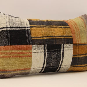 May include: A rectangular patchwork cushion with a black, white, orange, and brown plaid pattern. The cushion is made of woven fabric and has a soft, textured surface.