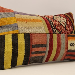 Puede incluir: Una almohada rectangular de patchwork con una variedad de rayas coloridas y patrones geométricos en tonos de rojo, amarillo, azul, negro y blanco.