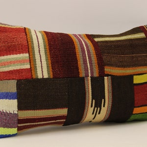 May include: A rectangular cushion with a patchwork design. The cushion is made of different coloured fabrics, including red, brown, green, yellow, and blue. The fabric is woven with stripes and geometric patterns.