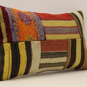 May include: A colorful patchwork pillow with stripes and geometric patterns in shades of red, orange, yellow, brown, black, and purple.