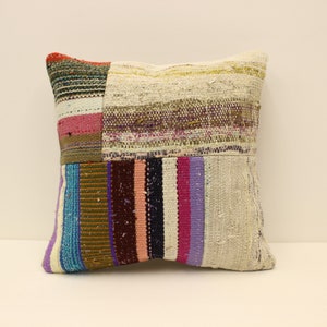 May include: A square throw pillow with a patchwork design. The pillow is made of different coloured fabrics, including white, blue, pink, purple, and brown. The fabric is woven with stripes and has a rustic, handmade look.